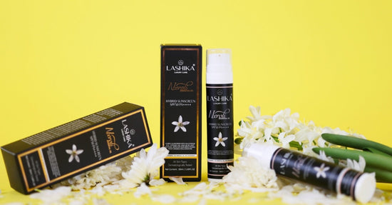 Image of Lashika Neroli Hybrid Sunscreen SPF 50 PA++++ displayed with its elegant black and gold packaging. The scene includes white neroli flowers and green stems scattered artistically against a vibrant yellow background.